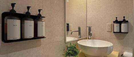 Une salle de bain moderne avec un grand miroir, un lavabo et trois bouteilles de shampoing posées sur une étagère.