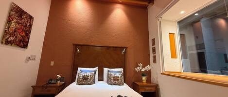 Un dormitorio con techo de madera, una cama grande con almohadas estampadas, una mesita de noche con teléfono y una ventana con vistas.