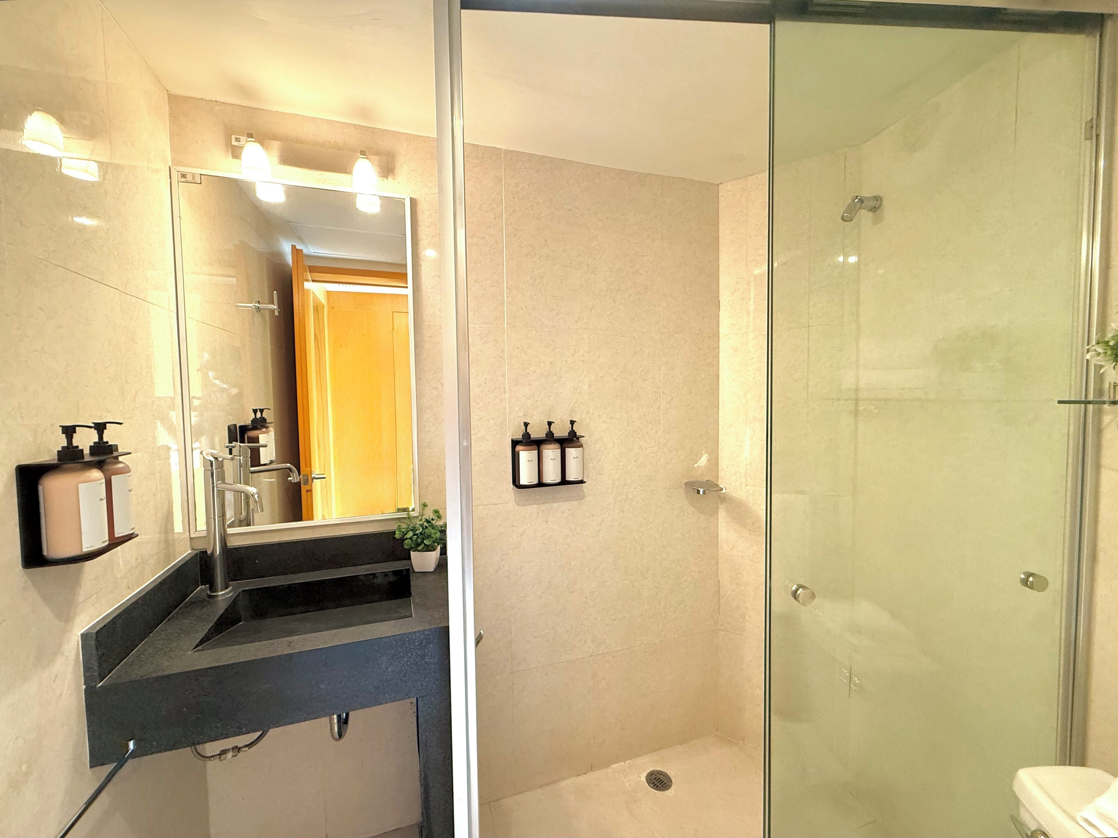 Un baño moderno con cabina de ducha de vidrio, lavamanos con espejo y artículos de aseo en la pared.