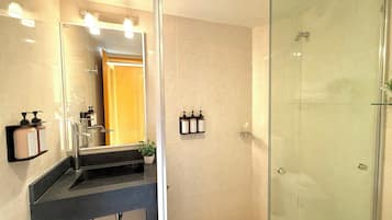 Un baño moderno con cabina de ducha de vidrio, lavamanos con espejo y artículos de aseo en la pared.