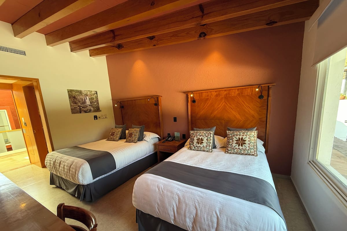 A hotel room with two beds, wooden headboards, and a large window.