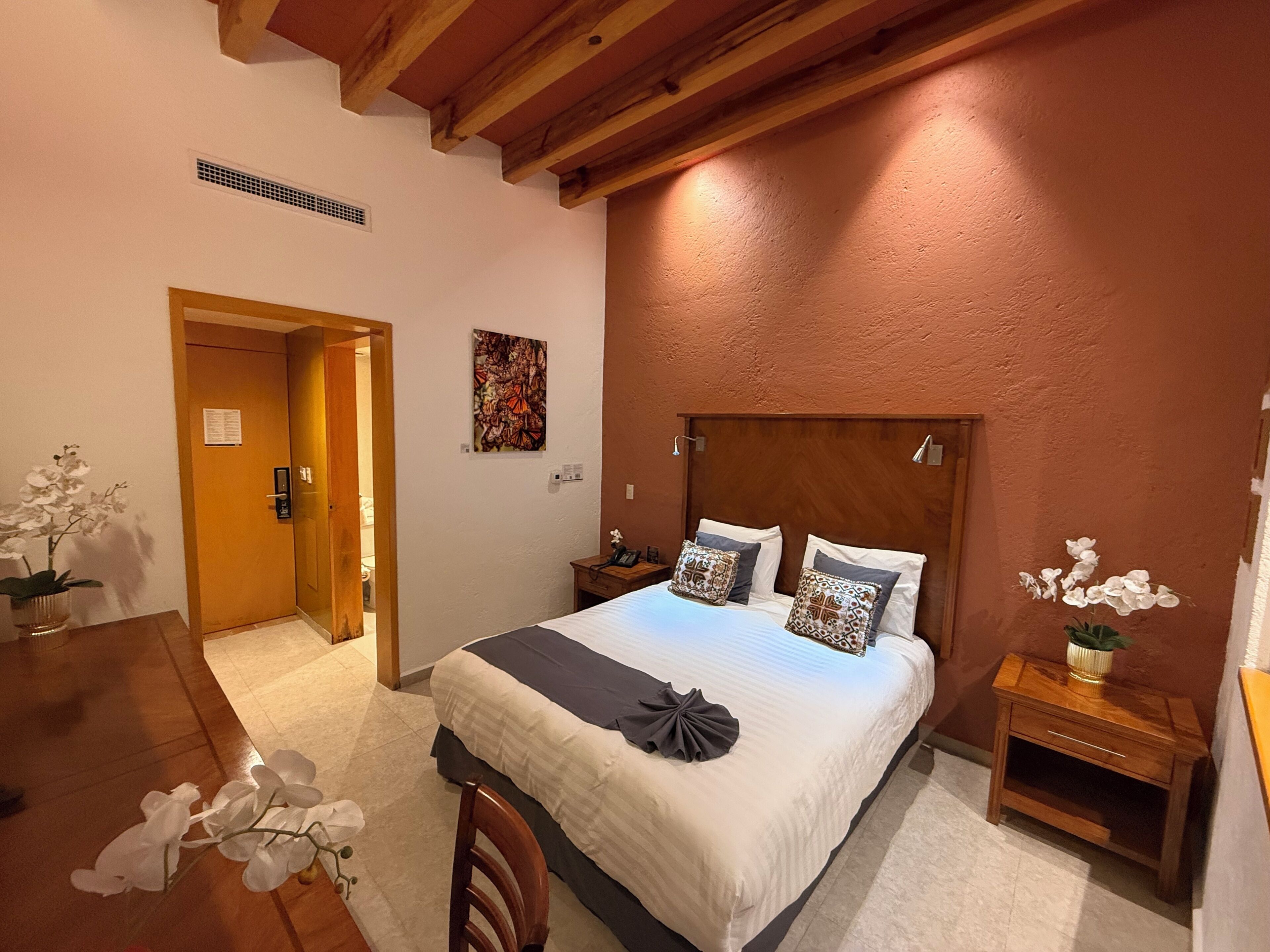 A bedroom with a bed, wooden headboard, bedside tables, a nightstand, a desk, and a chair.