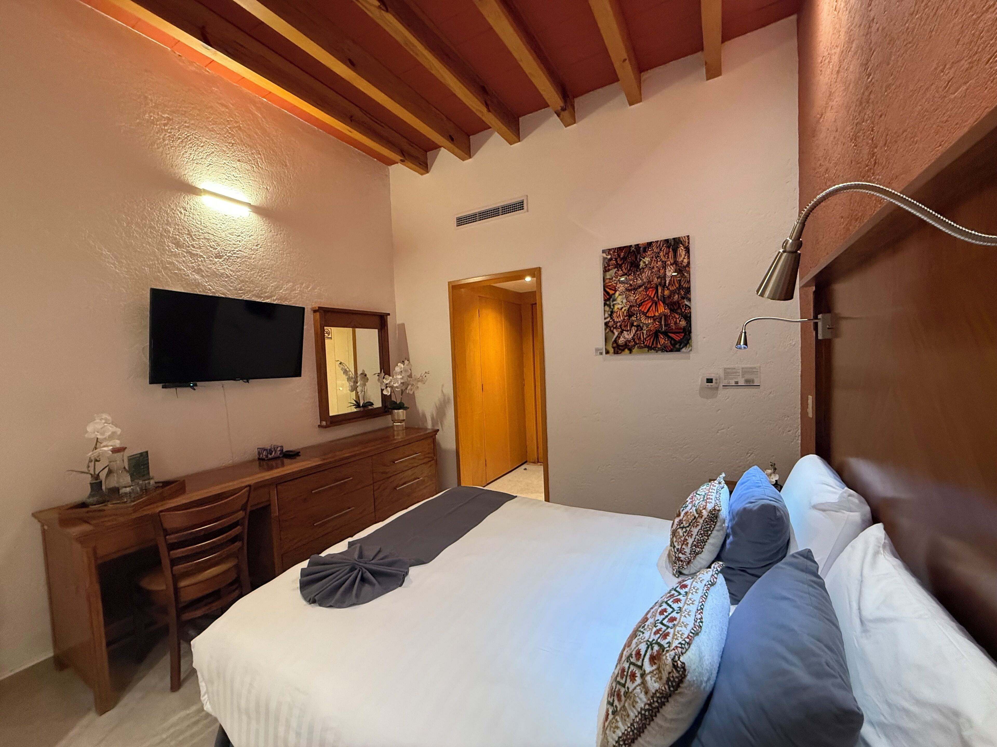 A hotel room with a bed, a desk, a chair, a television, a mirror, and a door.