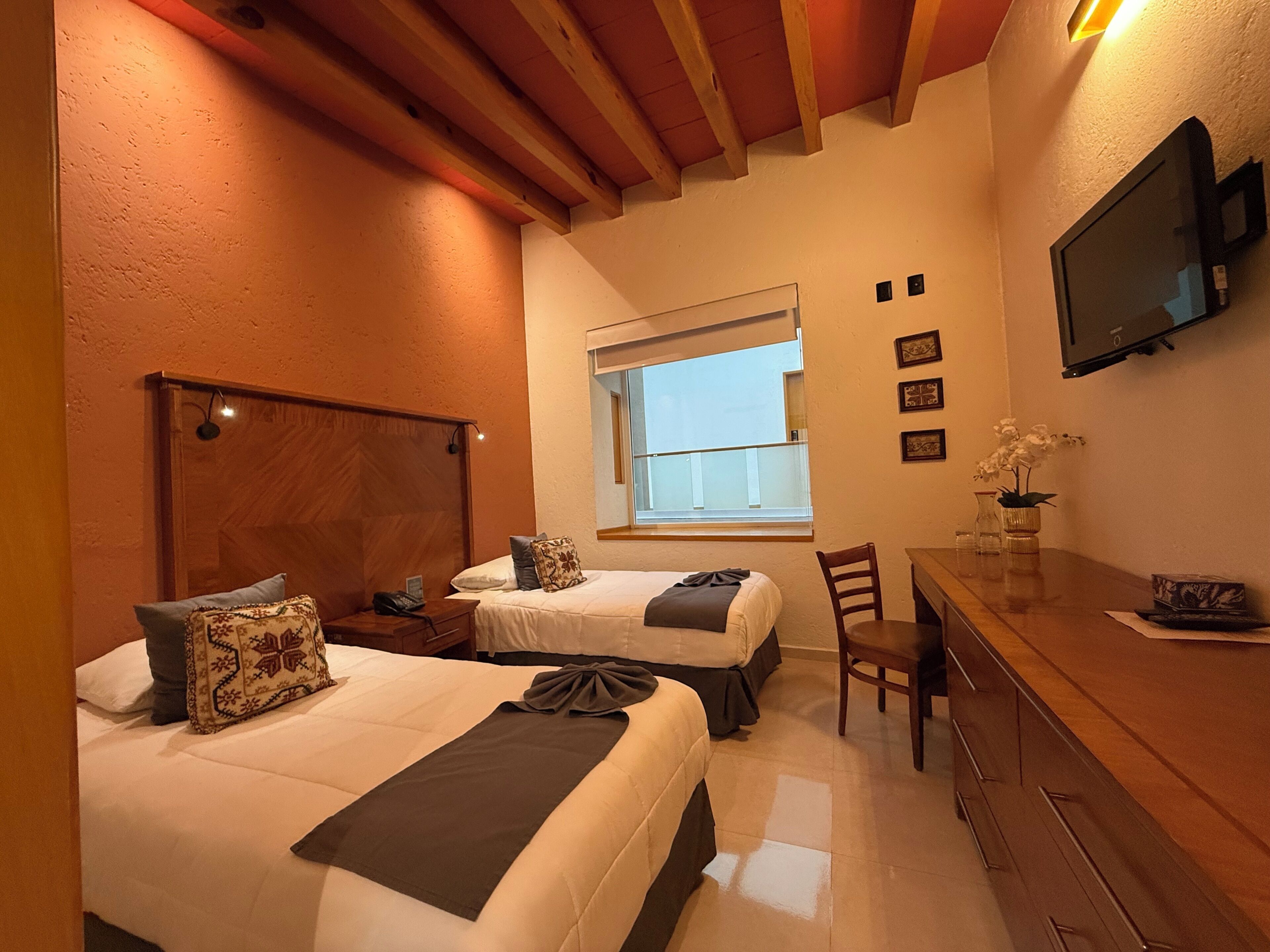 A hotel room with two beds, a desk, a chair, a TV, and a window with a view.
