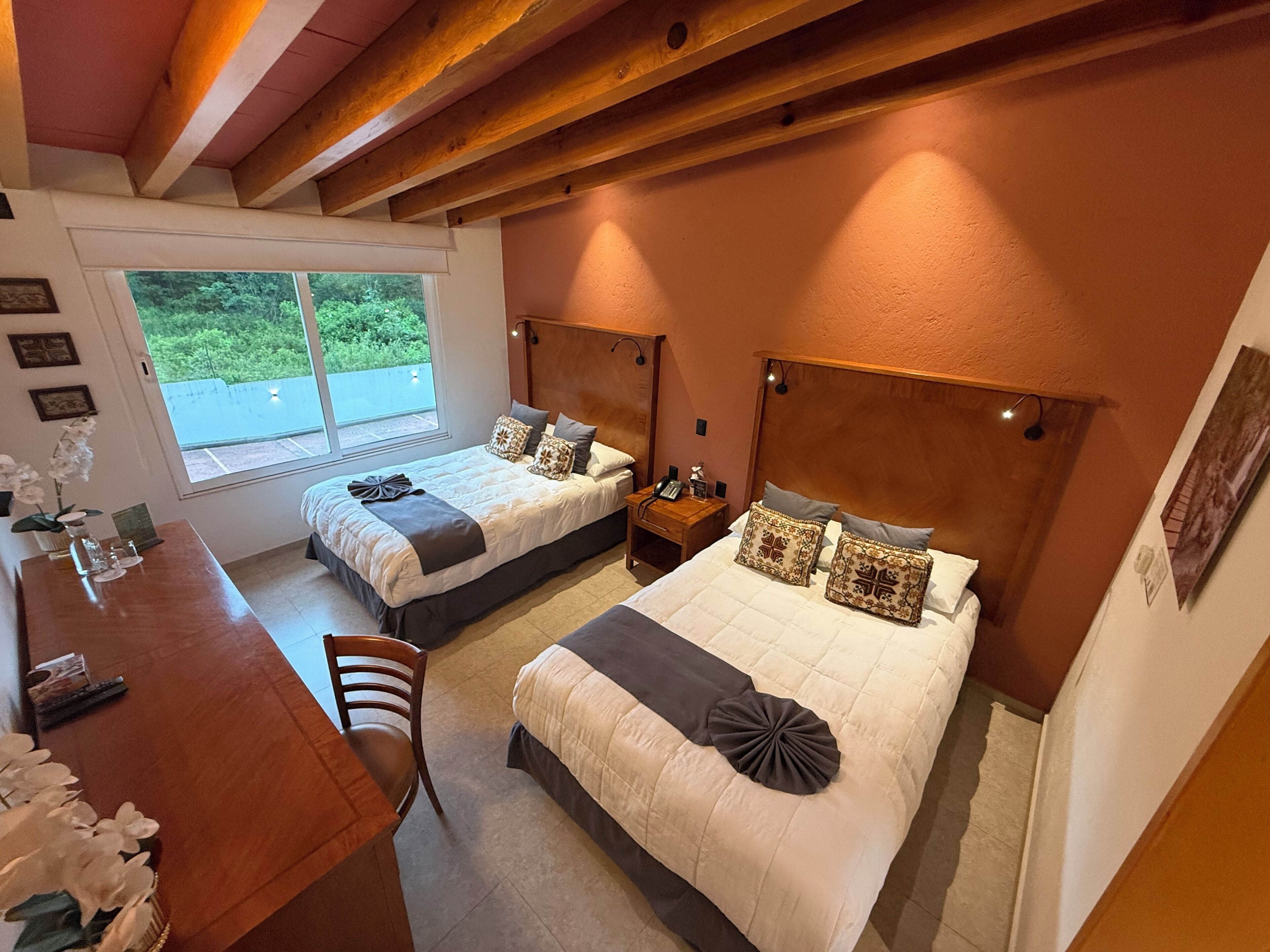A hotel room with two beds, a wooden desk, and a chair.