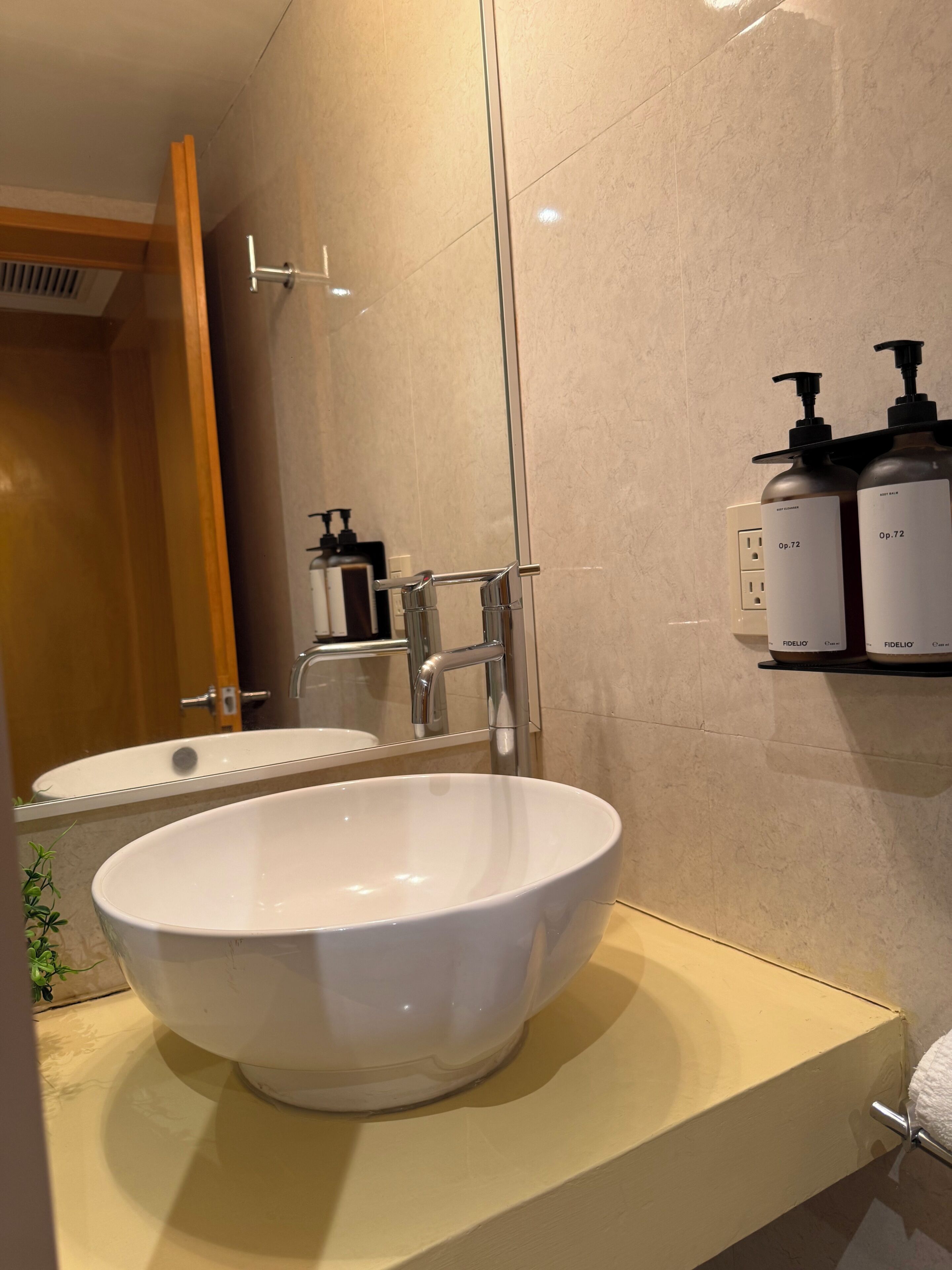 A bathroom with a white sink, a mirror, a glass shower enclosure, and toiletries on a shelf.