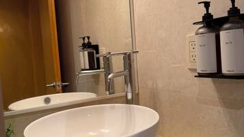 A bathroom with a white sink, a mirror, a glass shower enclosure, and toiletries on a shelf.