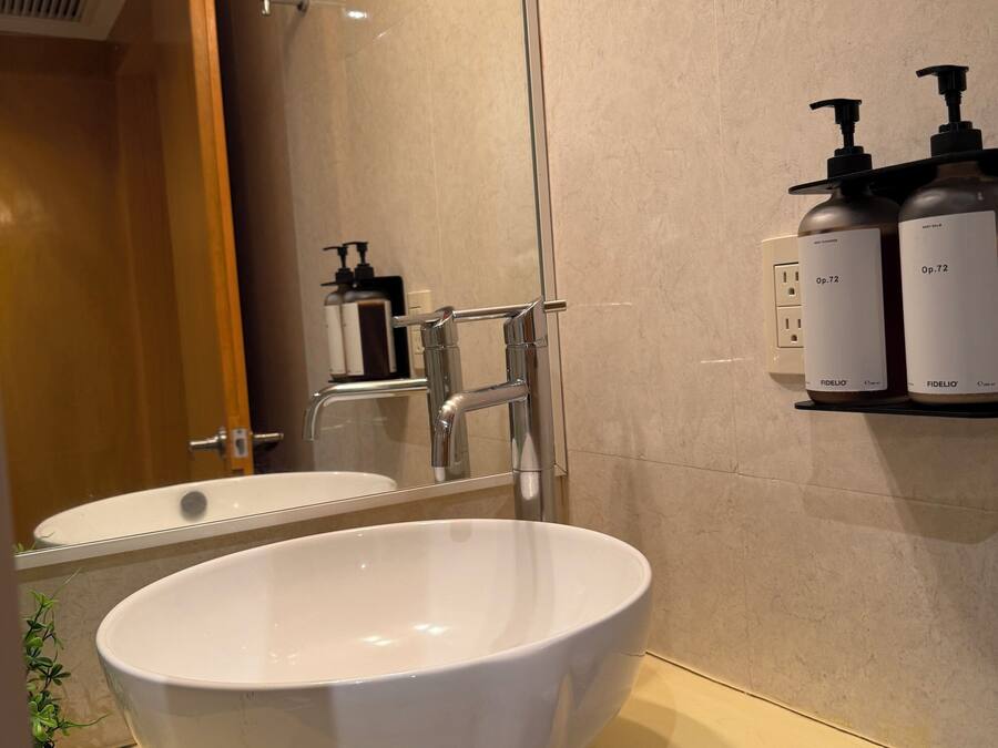 A bathroom with a white sink, a mirror, a glass shower enclosure, and toiletries on a shelf.