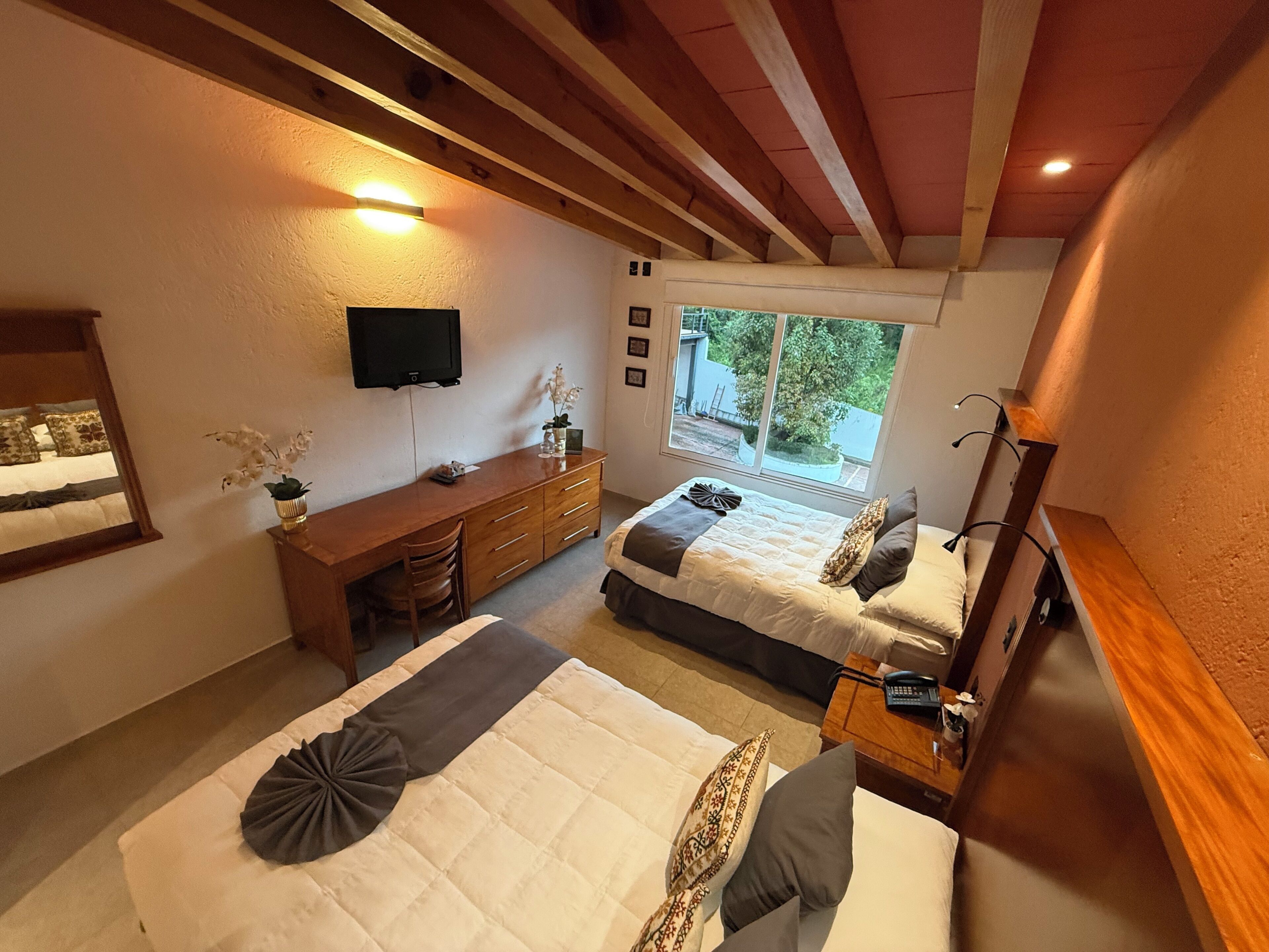 Quarto com duas camas, uma escrivaninha, televisão e janela com vista para o exterior.