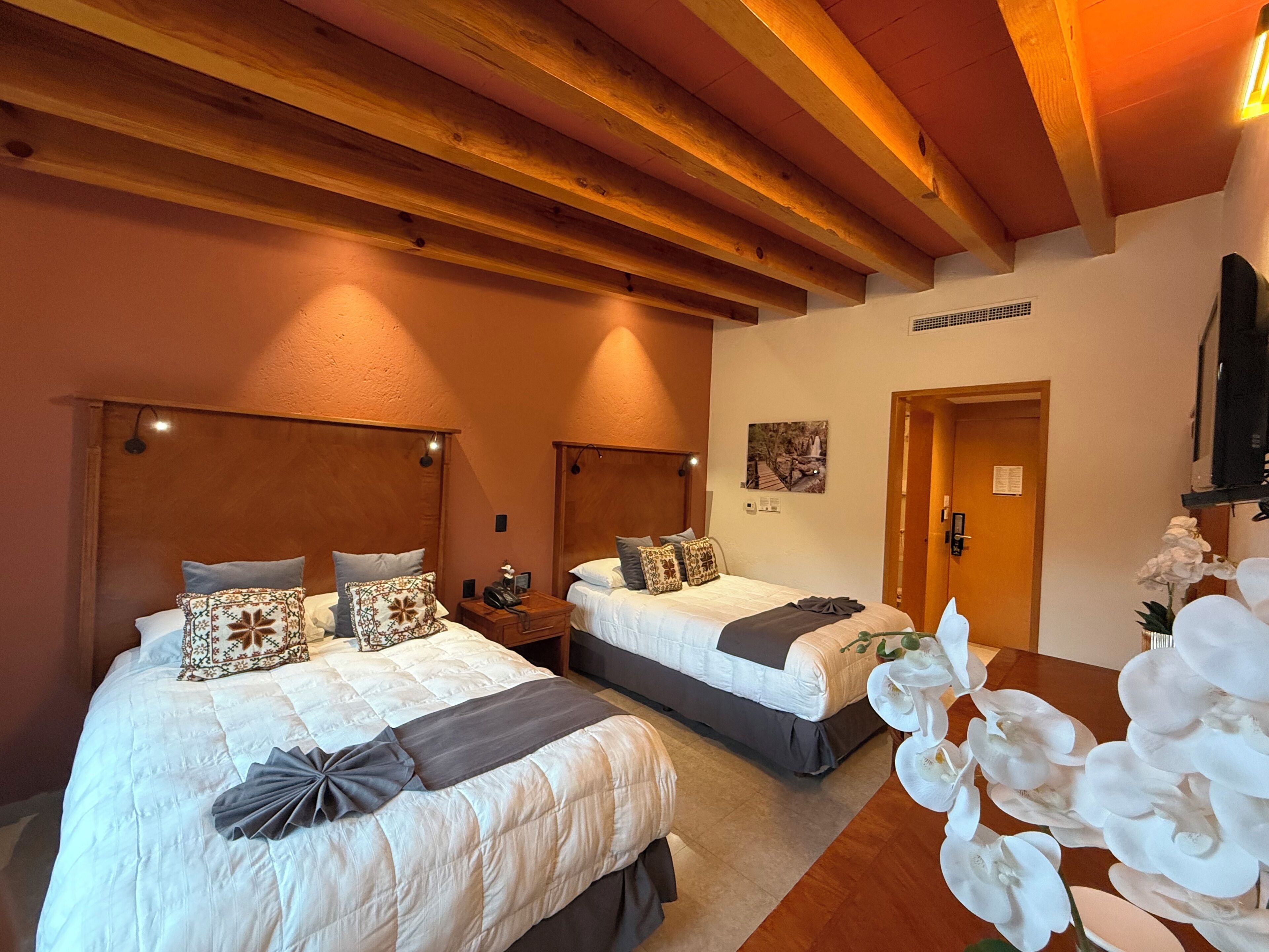 A hotel room with two beds, wooden beams on the ceiling, a door, and a wall-mounted picture.
