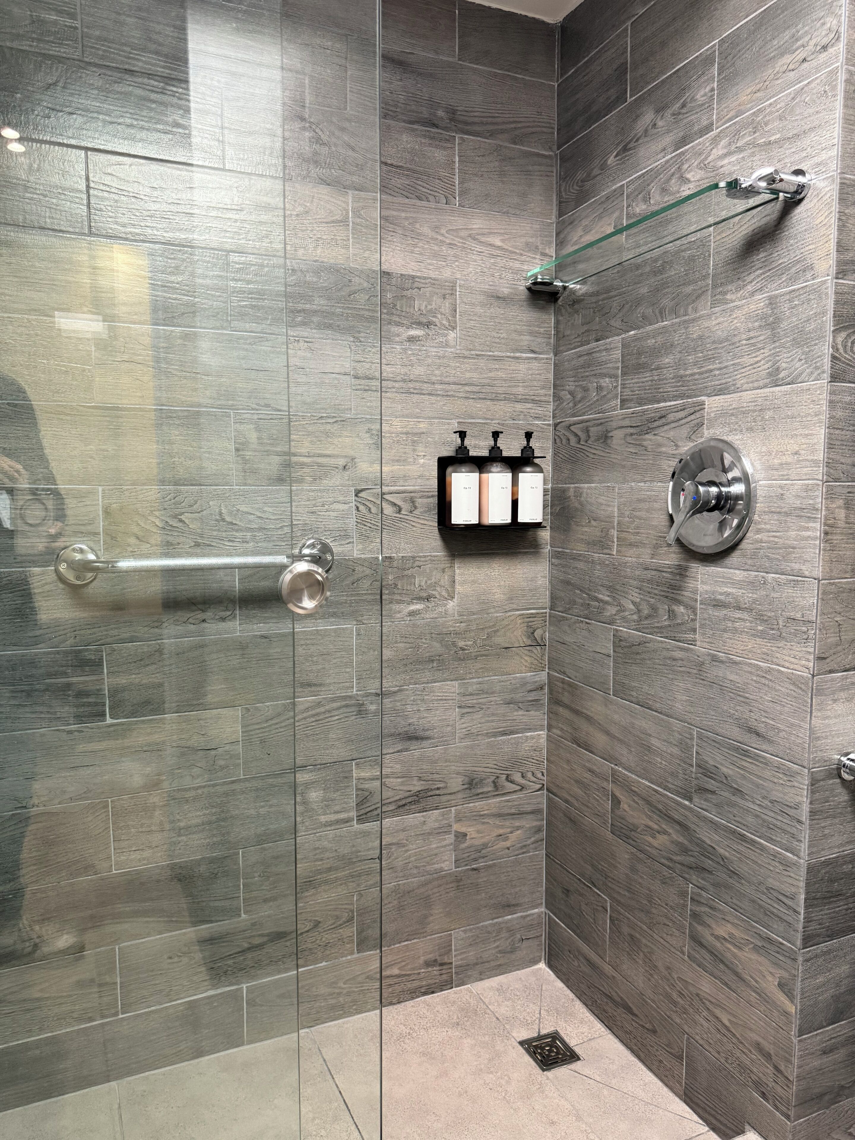 A shower area with a glass door, a hand dryer, and a soap dispenser mounted on the wall.
