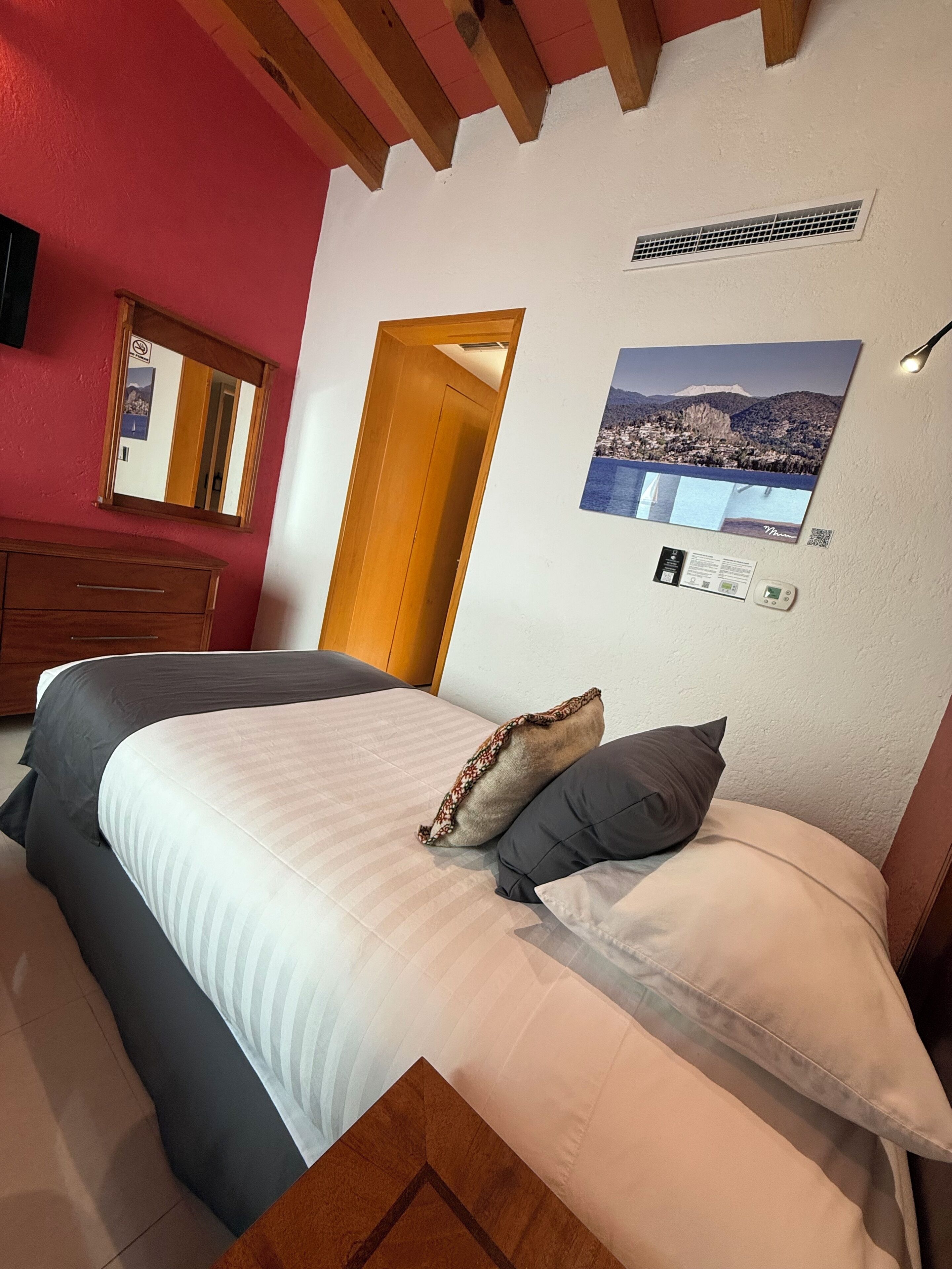 Un dormitorio con cama, cabecera de madera, espejo, puerta y aire acondicionado instalado en la pared.
