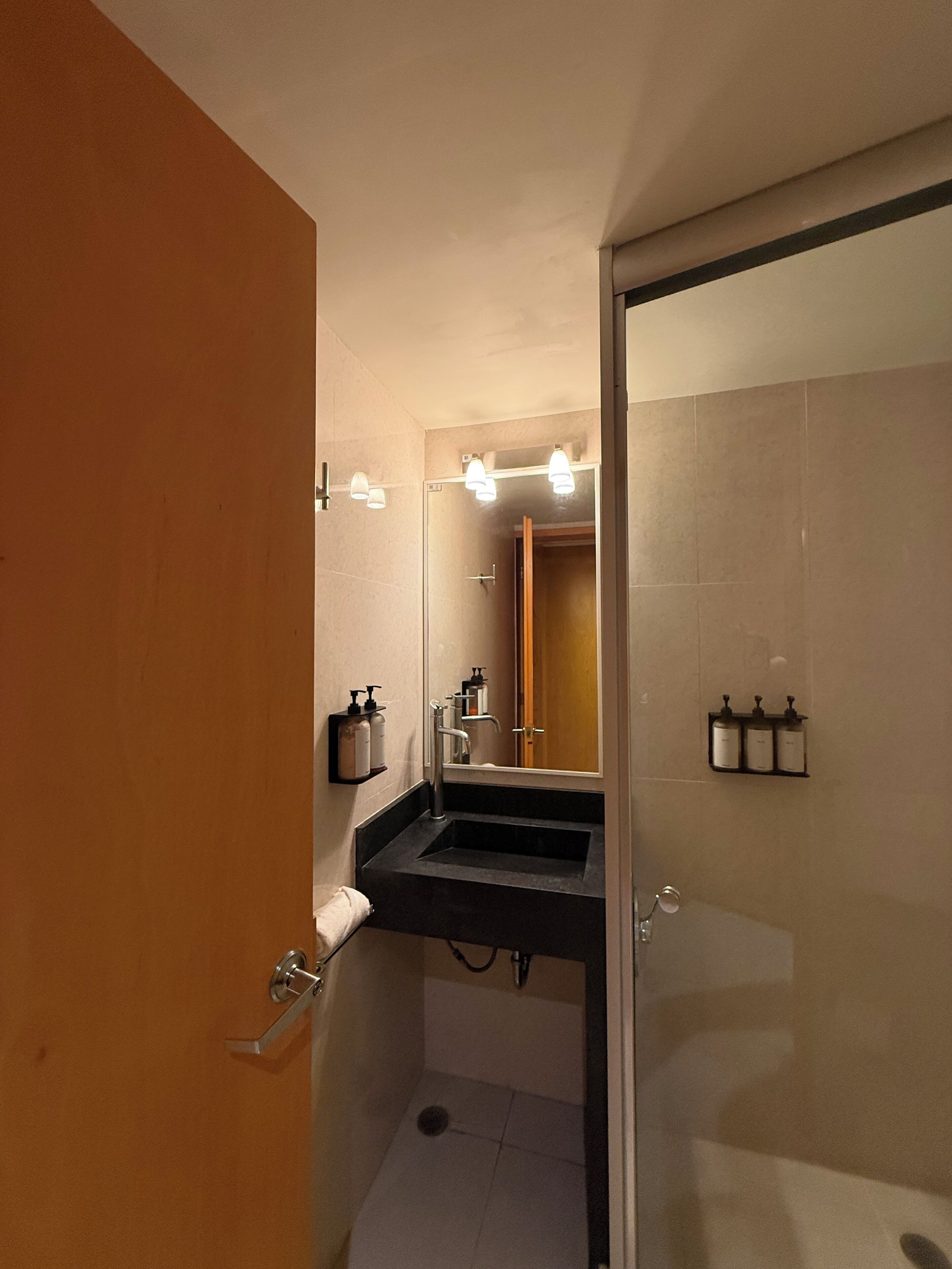 Un baño con un lavabo negro, un espejo y dos dispensadores de jabón en la pared.