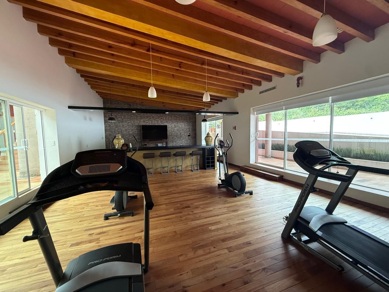 Een sportschool met trainingsapparatuur, een bar en grote ramen.