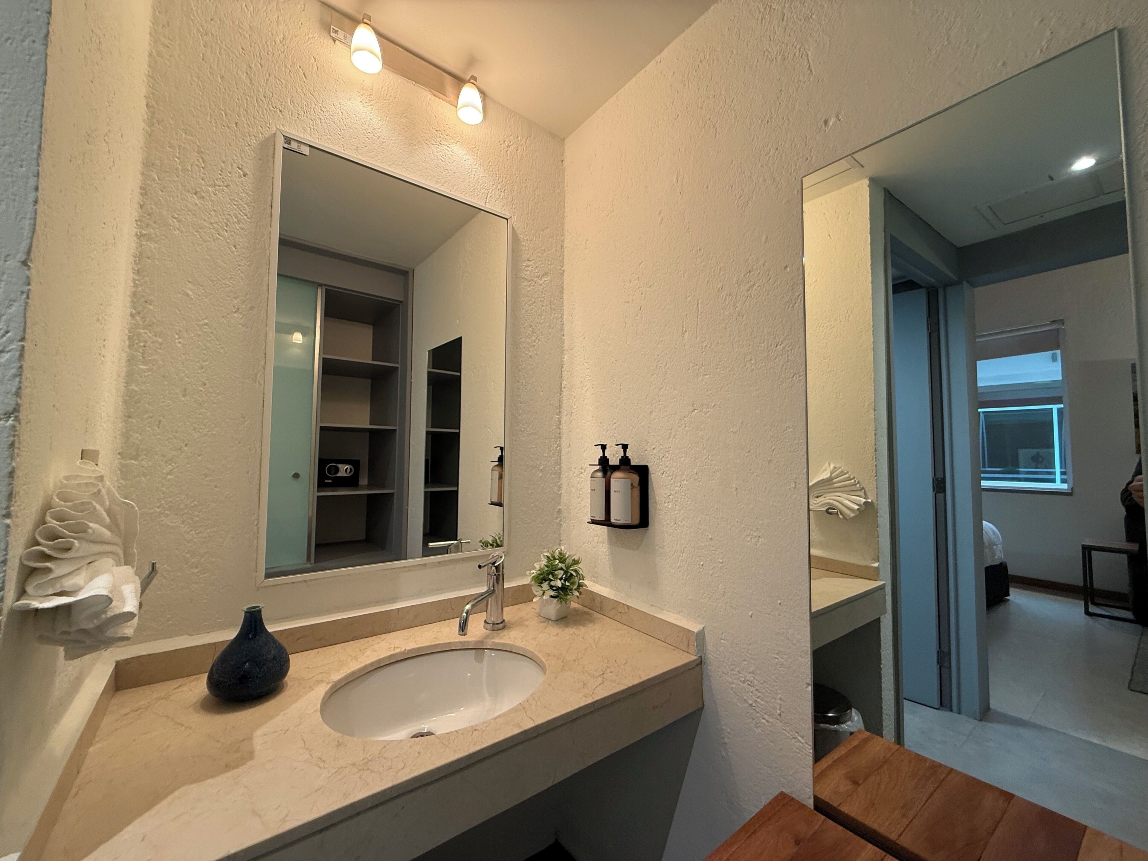 A bathroom with a large mirror, a sink, and a shelf with toiletries.