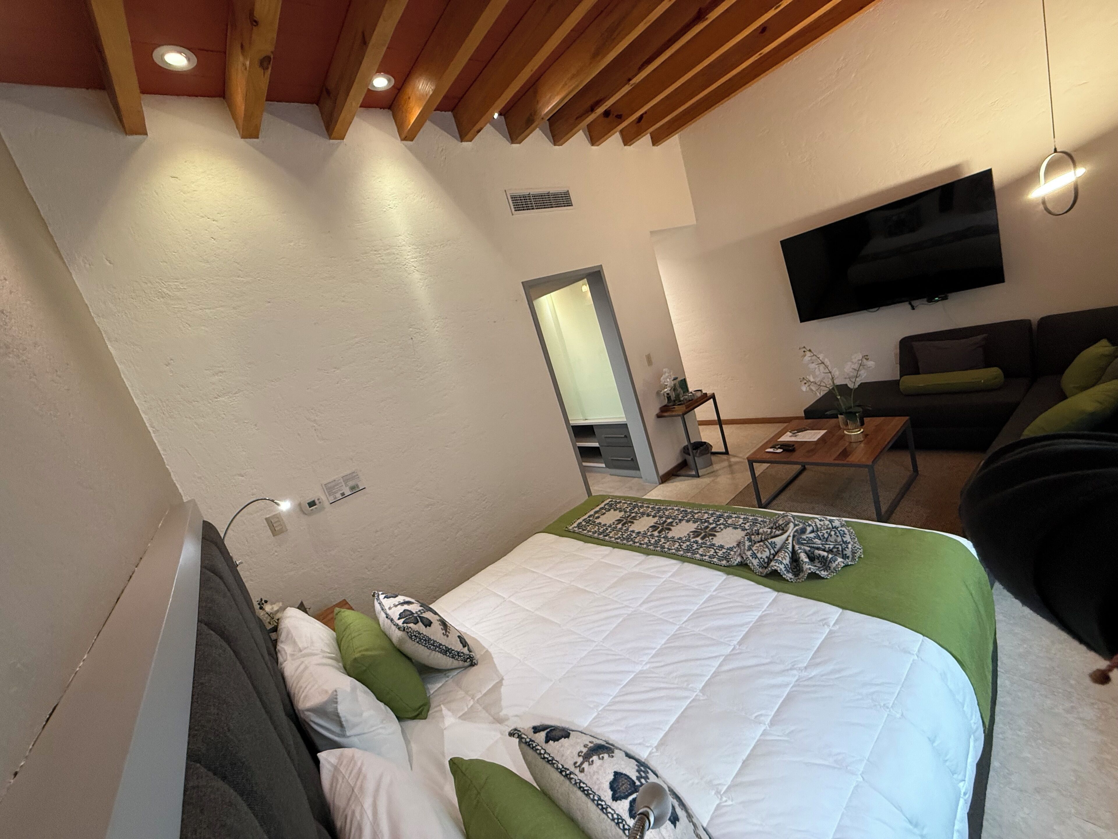 A bedroom with a bed, a TV mounted on the wall, a sofa, and a small table.