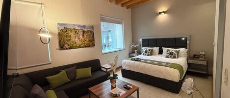 Un dormitorio moderno con una cama grande, un sofá, una mesita de centro y un cuadro en la pared.