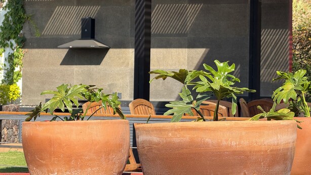 Un patio al aire libre con macetas de terracota, sillas de madera y una moderna área de cocina exterior.