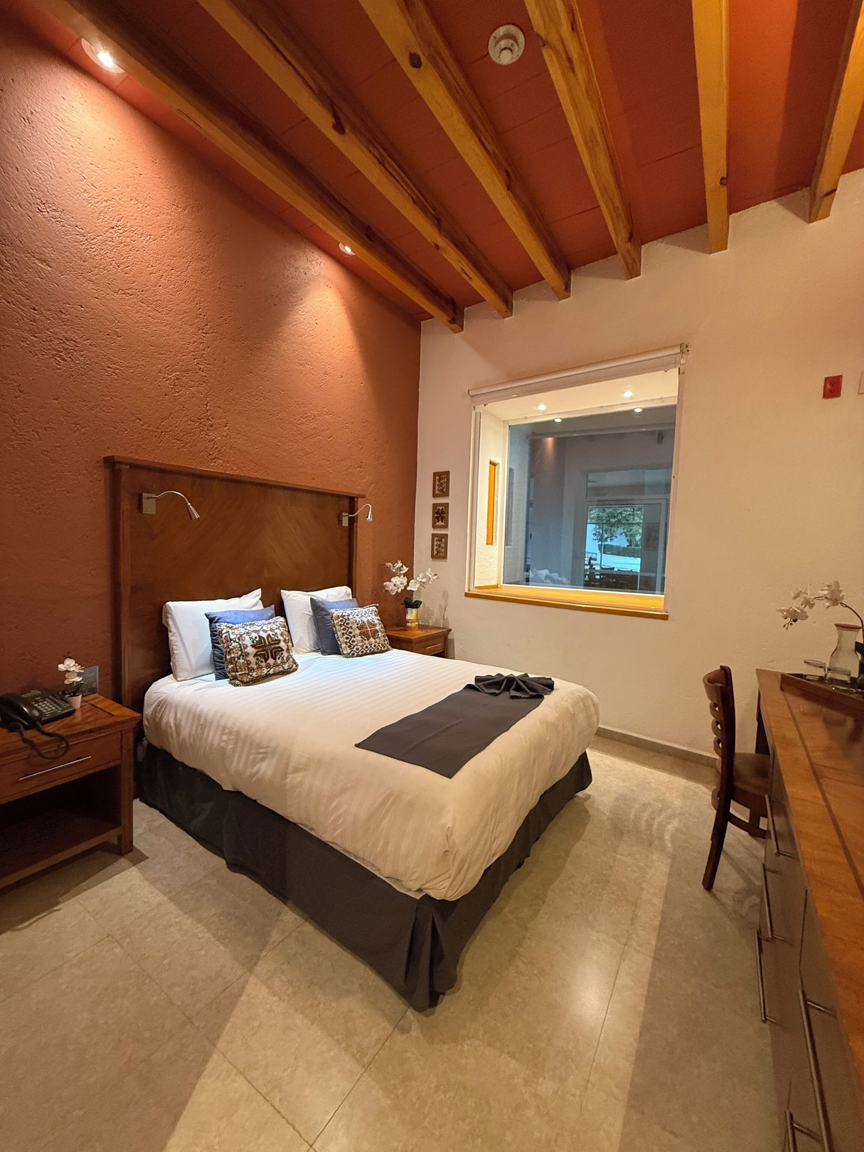 A bedroom with a bed, bedside tables, a window, and a wooden ceiling.