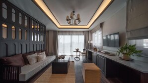A modern living room with a sofa, a coffee table, and a TV. There is a kitchen area with a counter and a plant. - Burirattana (Chiang Mai)