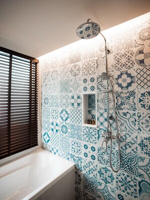Un baño con una bañera blanca, ducha con cabezal de ducha manual y ventana con persianas.