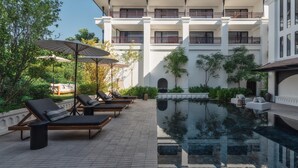 A poolside area with lounge chairs and umbrellas, a reflecting pool, and a multi-story building with balconies. - Burirattana (Chiang Mai)