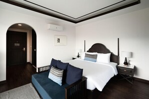 A hotel room with a large bed, a bedside table with a lamp, a small desk, and a chair. - Burirattana (Chiang Mai)
