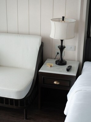A hotel room with a white upholstered sofa, a bedside table with a lamp, a remote control, and a 'No Smoking' sign. - Burirattana (Chiang Mai)