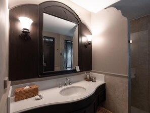 A bathroom with a large mirror, a white sink, and a glass shower enclosure. - Burirattana (Chiang Mai)