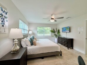 A bedroom with a bed, a ceiling fan, a dresser, a lamp, and a potted plant.