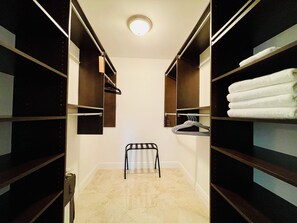 A walk-in closet with shelves, a chair, and hanging clothes.