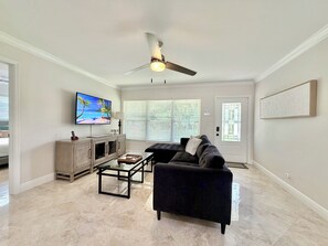 A living room with a dark sofa, a coffee table, a TV on the wall, and a ceiling fan.