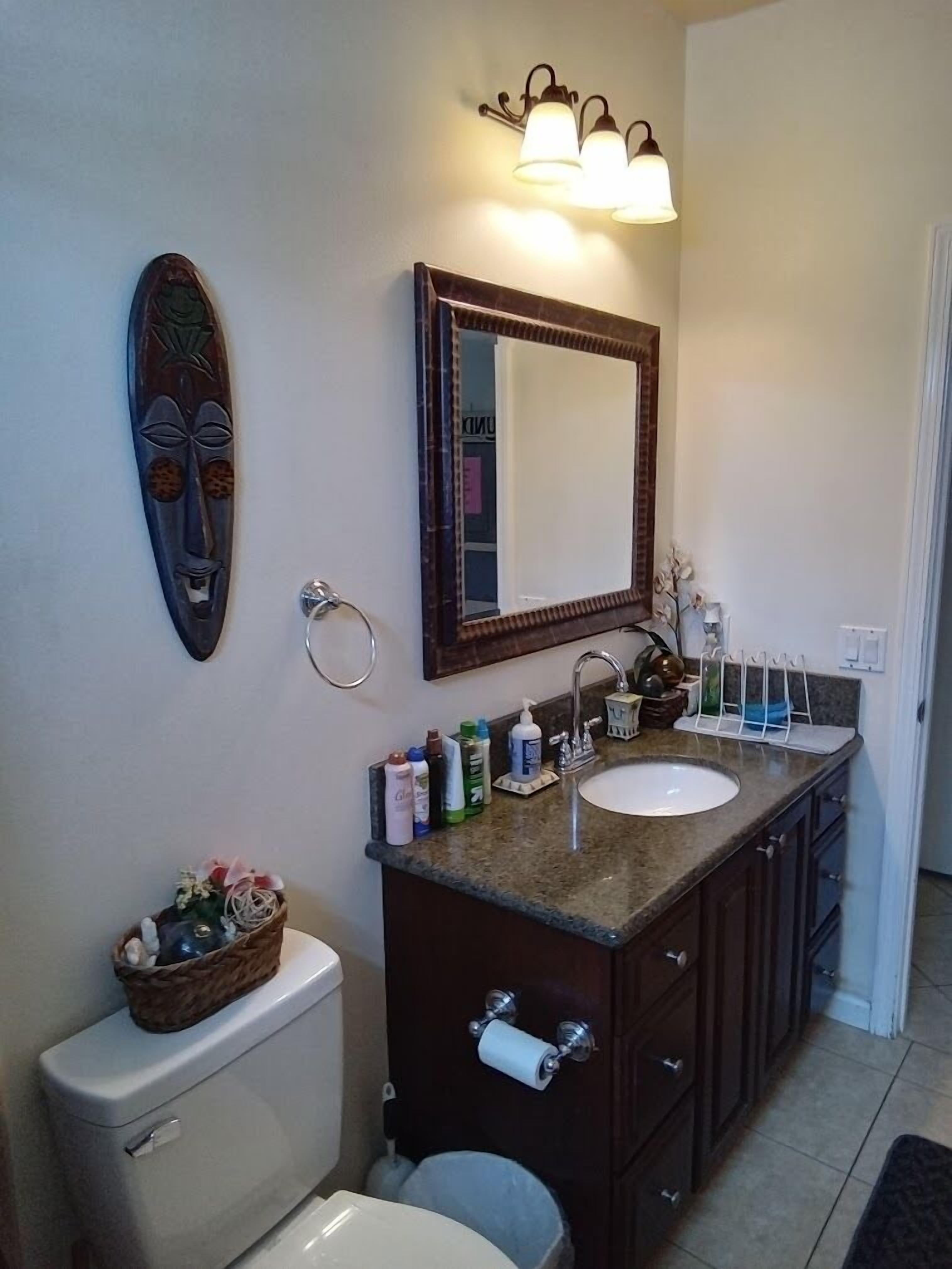 A bathroom with a toilet, sink, and mirror. There is a decorative item on the toilet and toiletries on the sink counter.
