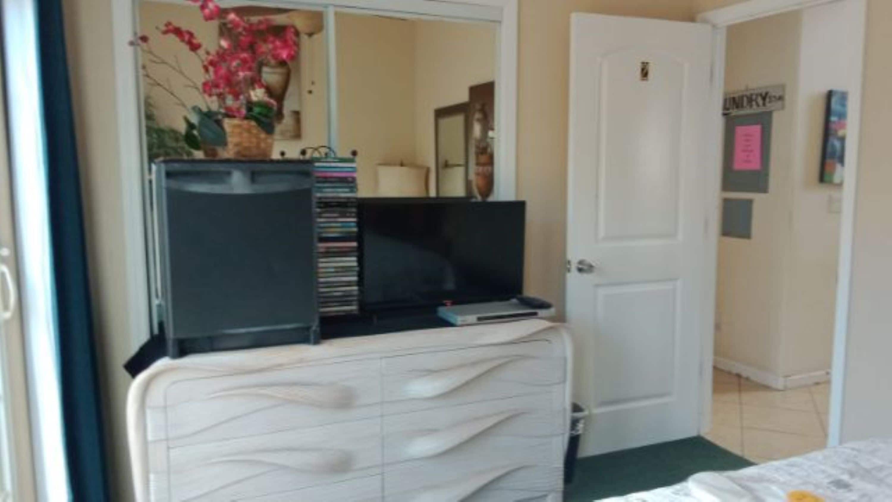 A bedroom with a white dresser, a television on top, and a door labeled "LINDY".