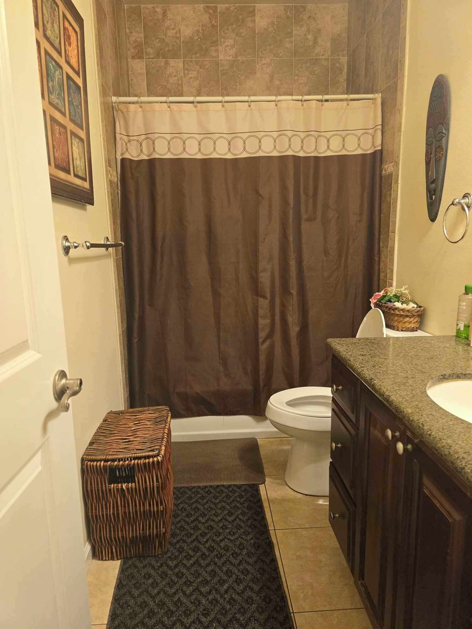A bathroom with a shower curtain, a toilet, a sink, and a small wicker basket.