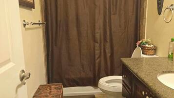 A bathroom with a shower curtain, a toilet, a sink, and a small wicker basket.