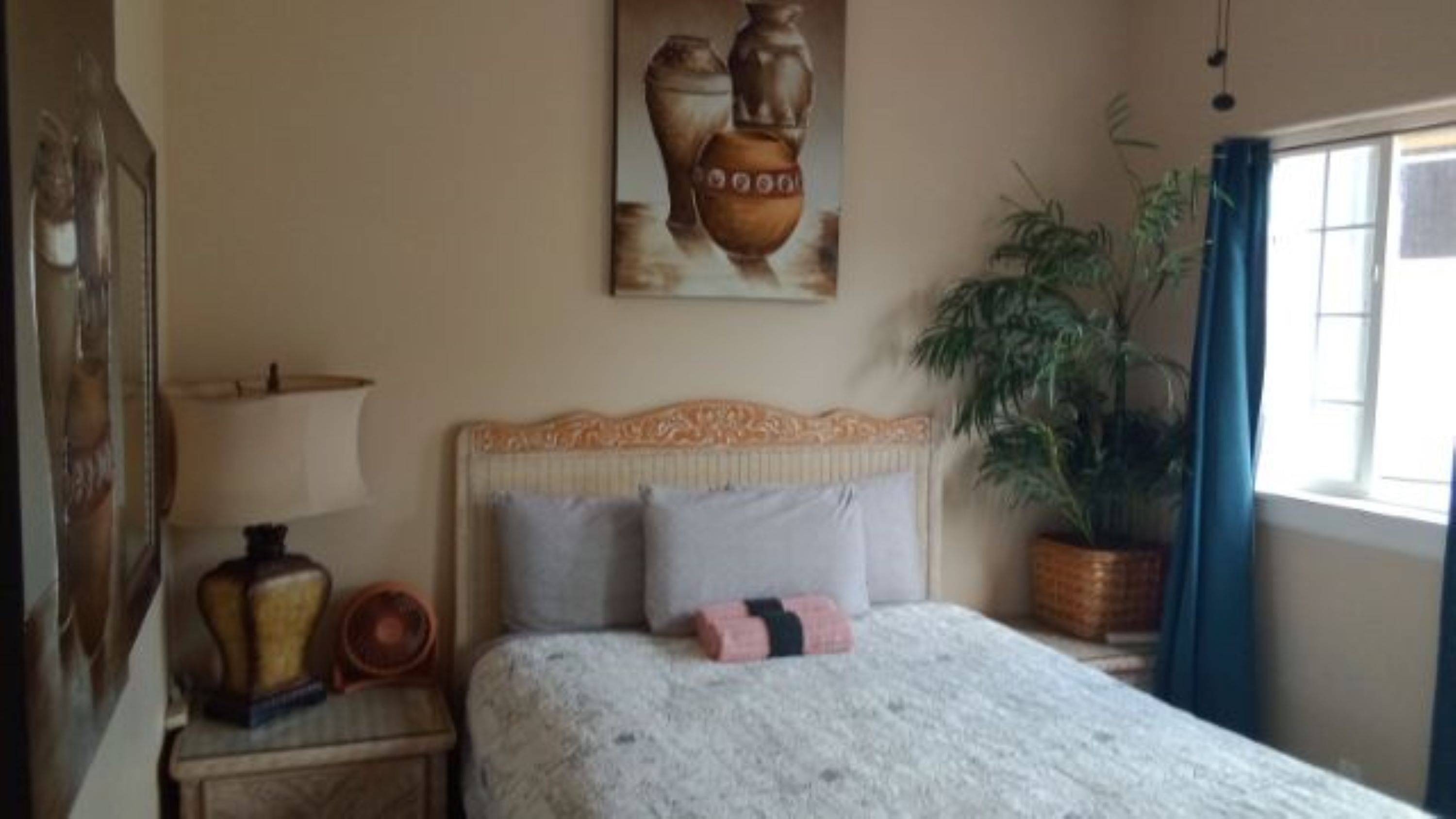 Une chambre à coucher avec un lit, une table de chevet, une lampe, un vase et une plante en pot.