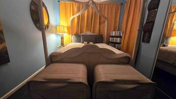 Une chambre avec un lit à baldaquin, une lampe de chevet, une bibliothèque et un miroir.