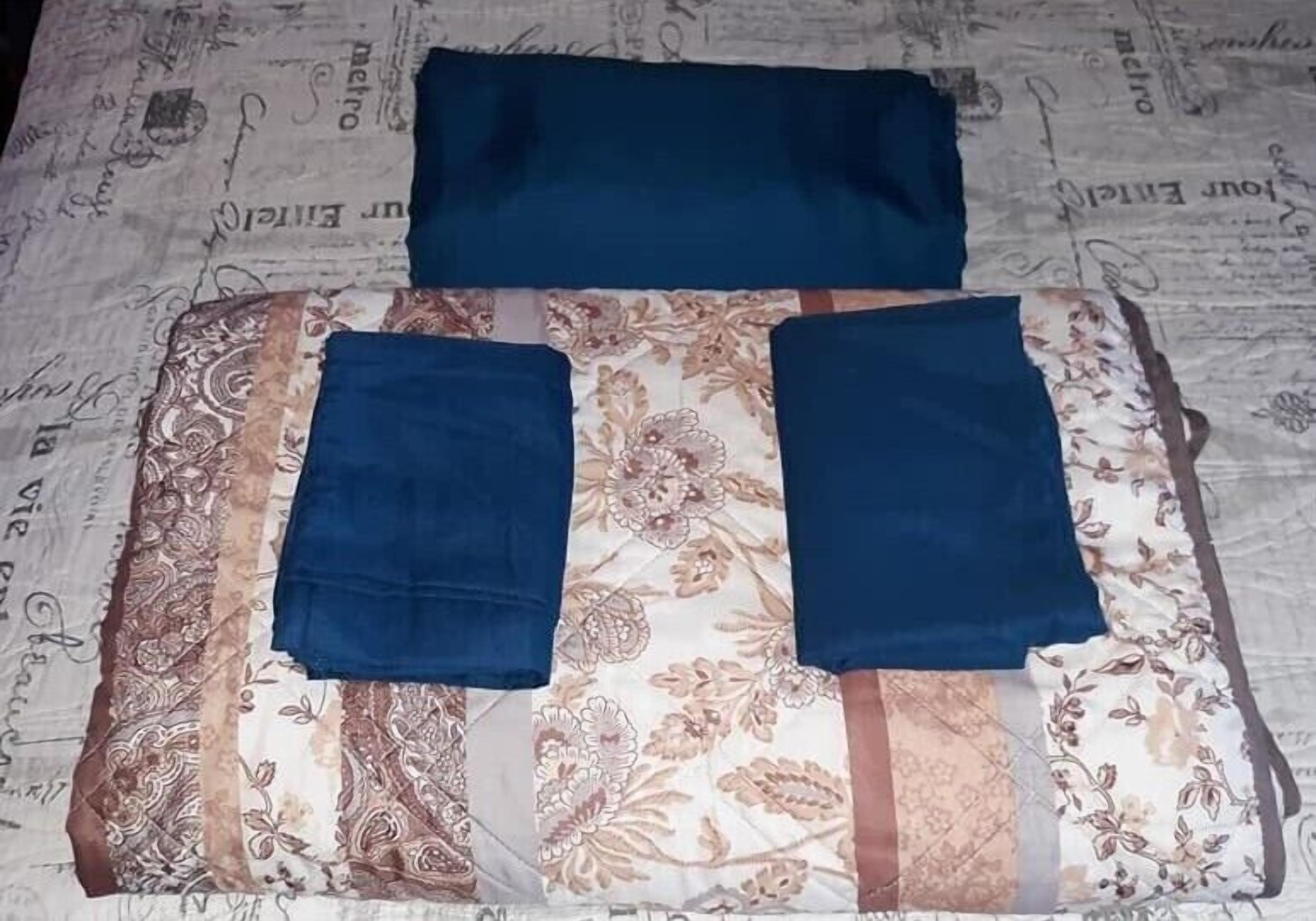 A bed with a floral patterned bedspread and two folded blue blankets.