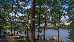A lakeside deck with outdoor seating and string lights. - Waterfront Cabin! Dock, Crab, Paddle, Kayak, Outdoor Movie, Karaoke, and More! (Heathsville)