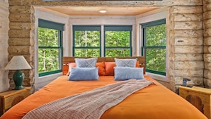 A log cabin room with a bed, a sign reading "Chesapeake Bay Inn", and large windows with a view of trees. - Waterfront Cabin! Dock, Crab, Paddle, Kayak, Outdoor Movie, Karaoke, and More! (Heathsville)