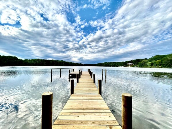 A wooden pier extending into calm water, surrounded by trees and a cloudy sky. - Waterfront Cabin! Dock, Crab, Paddle, Kayak, Outdoor Movie, Karaoke, and More! (Heathsville)