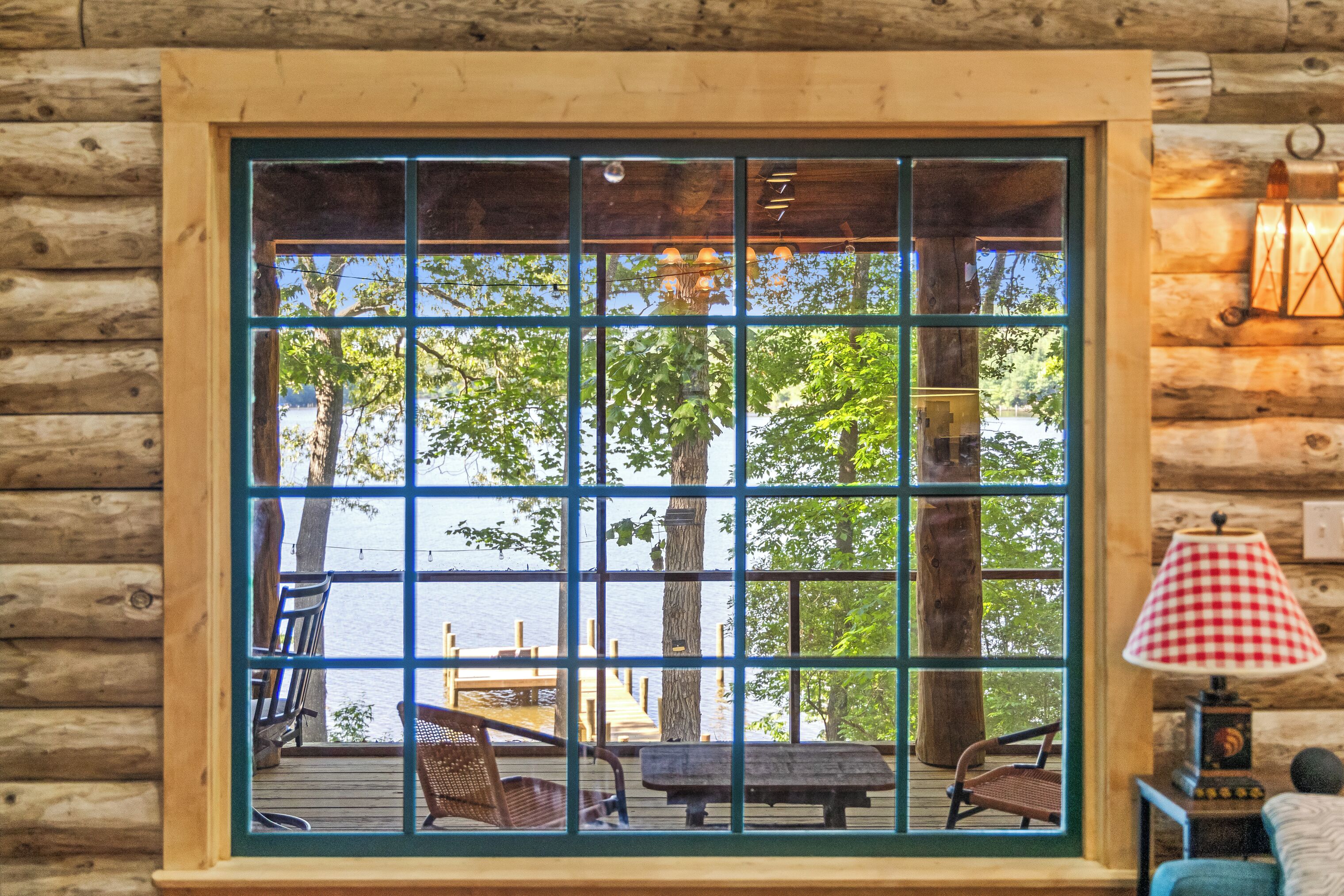 Une cabane dotée d’une grande fenêtre donnant sur un quai et l’eau, avec des murs en bois et une lampe placée à droite.