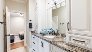 Une salle de bain avec des meubles blancs, un comptoir en granit, un grand miroir et un porte-serviettes avec des serviettes bleues.