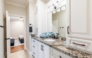 Un bagno con mobili bianchi, un piano di lavoro in granito, uno specchio grande e un portasciugamani con asciugamani blu.