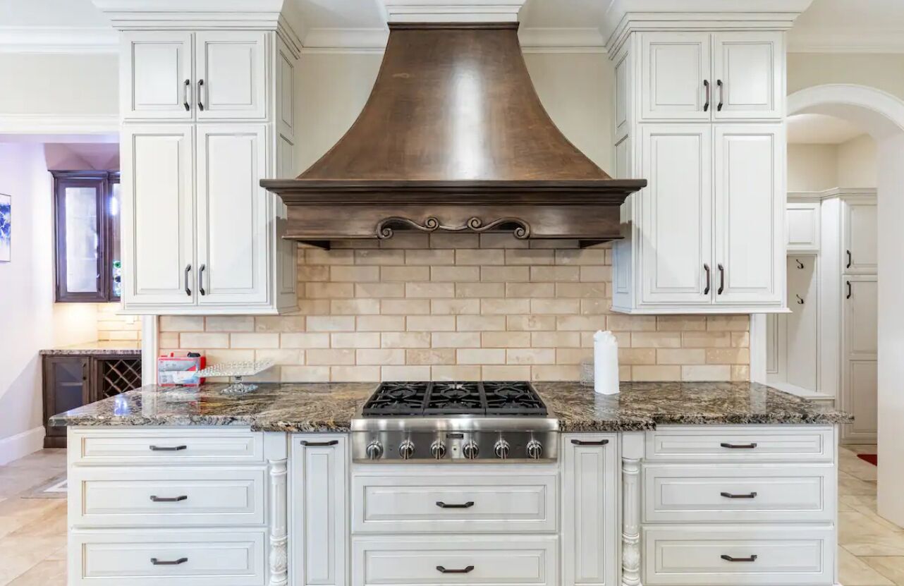 A kitchen with white cabinetry, a central stove, and a brick backsplash.