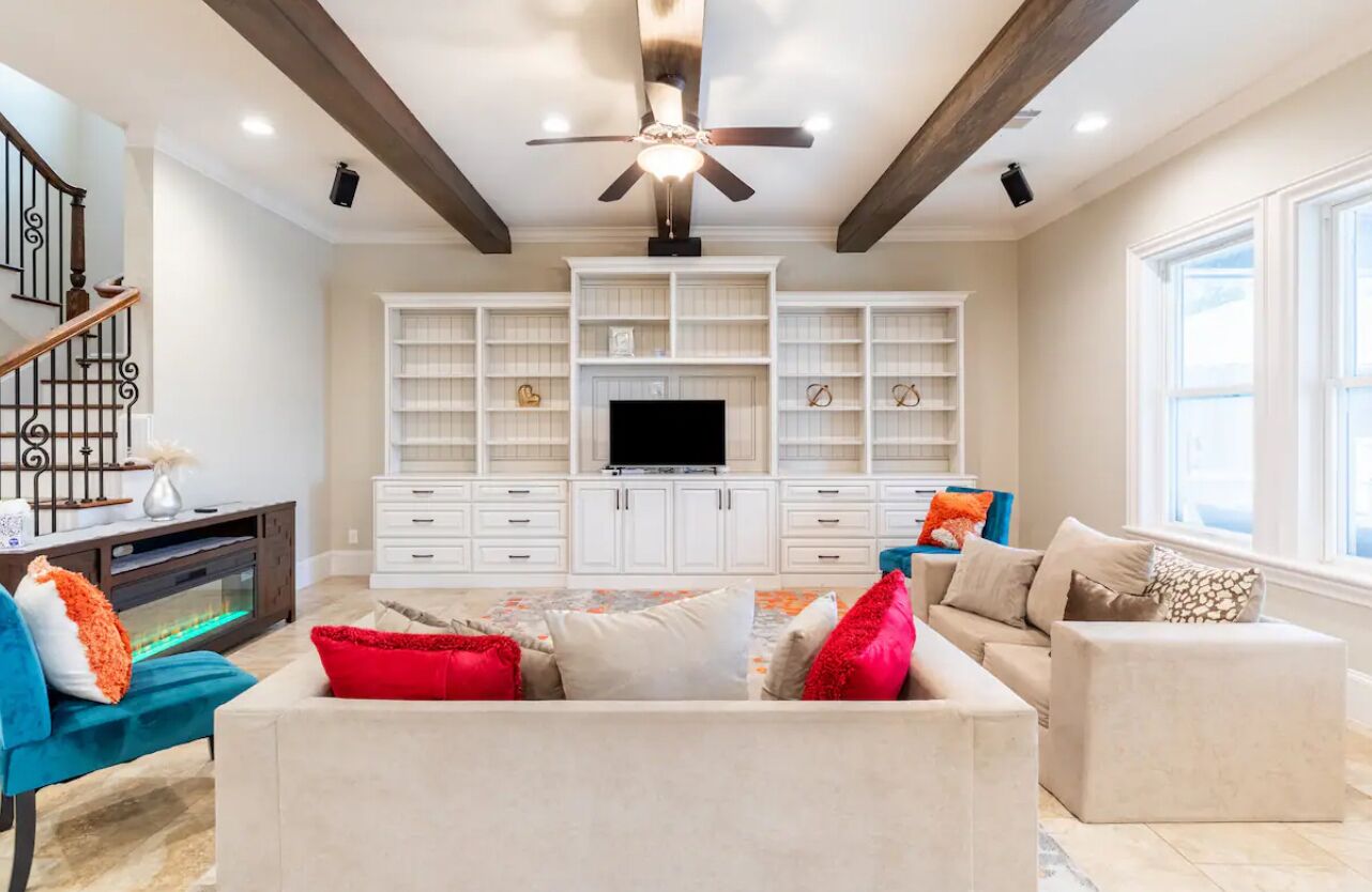 A spacious living room with a large TV, built-in shelving, and a ceiling fan.