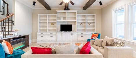 A spacious living room with a large TV, built-in shelving, and a ceiling fan.