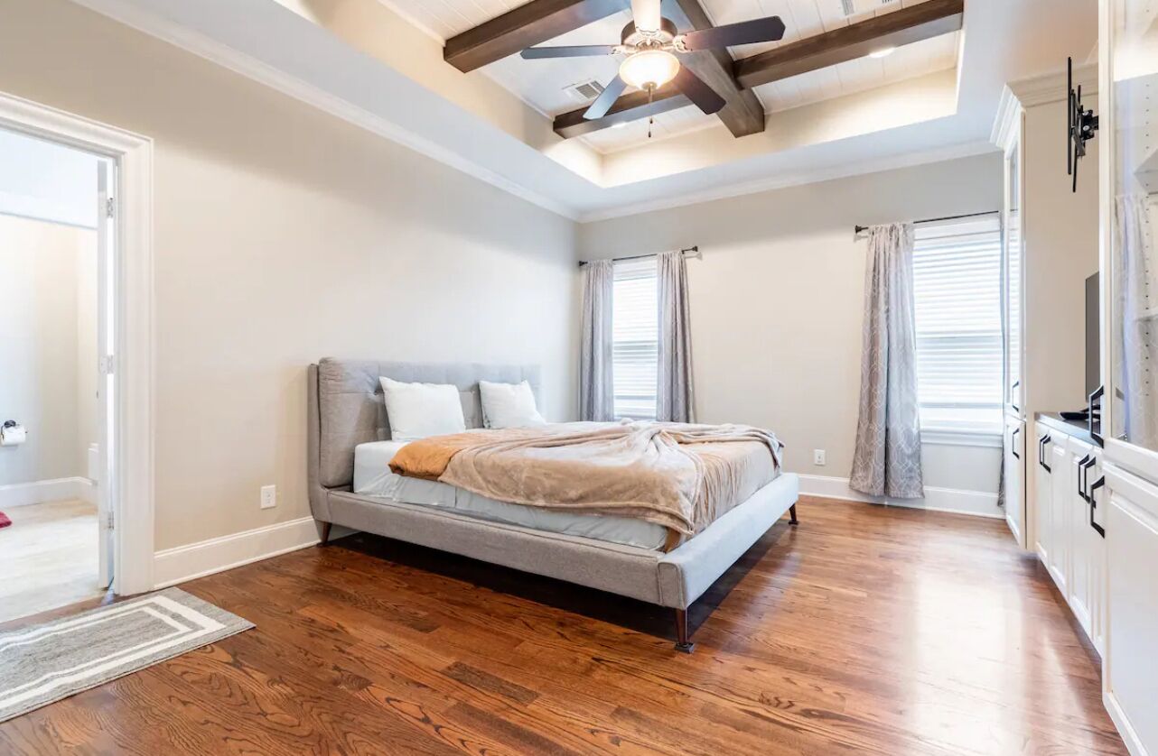 A bedroom with a bed, wooden flooring, a ceiling fan, and a window with curtains.