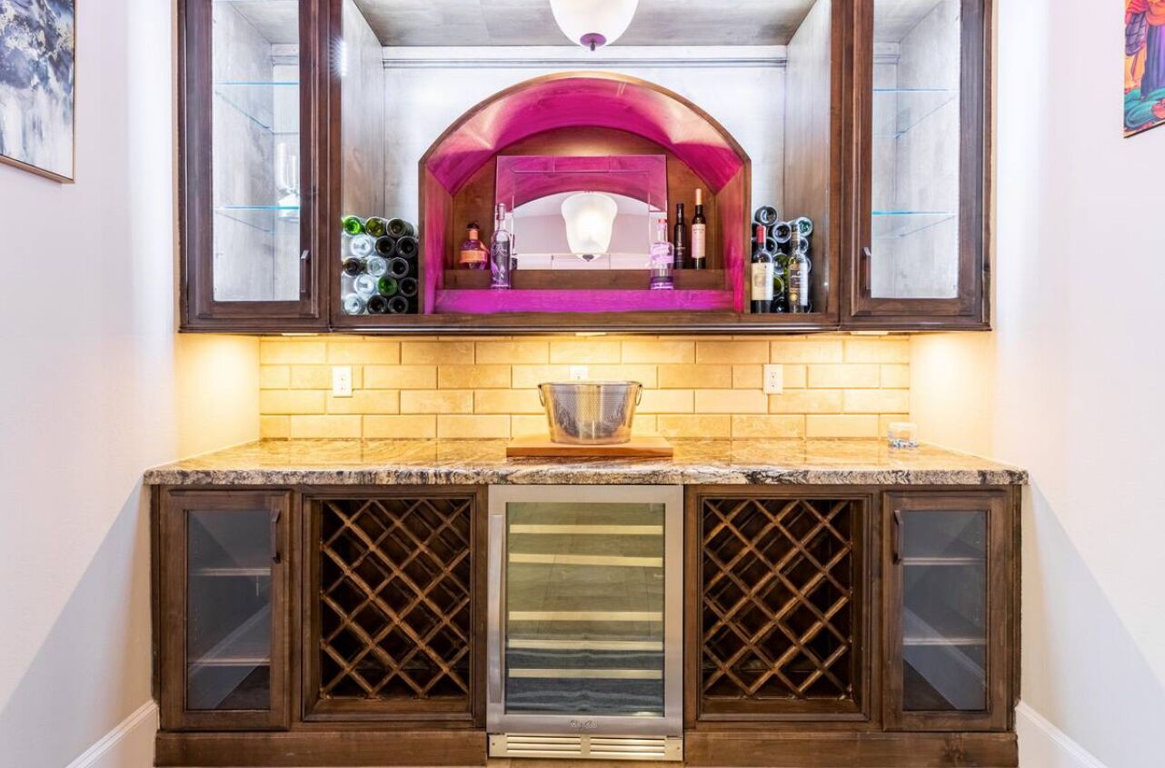 A kitchen with a built-in wine cooler, a pink arch above the sink, and a backsplash of yellow tiles.